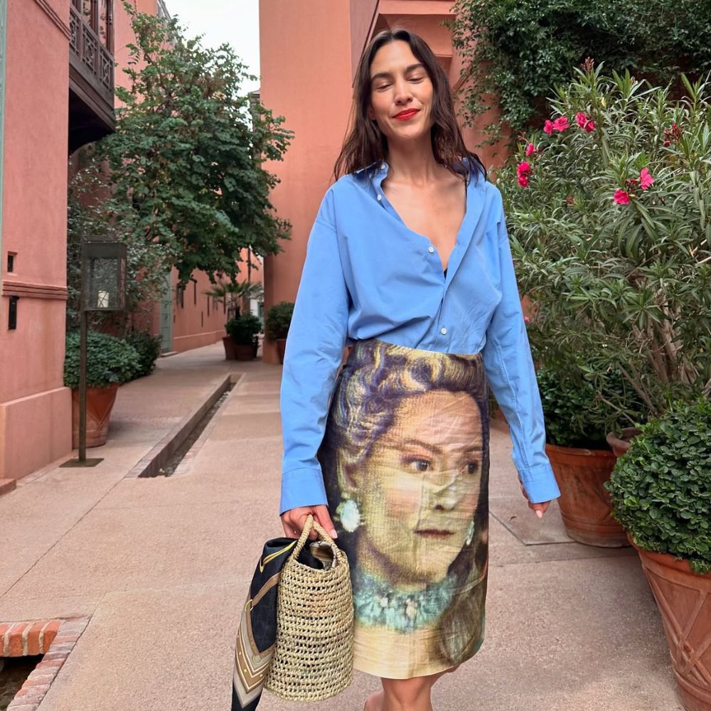Alexa Chung wears a blue button-down shirt with a printed skirt and raffia bag in Marrakech.
