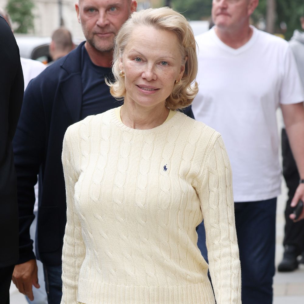Pamela Anderson walks outside in London wears a yellow knit and yellow maxi skirt with white and gold trainers.
