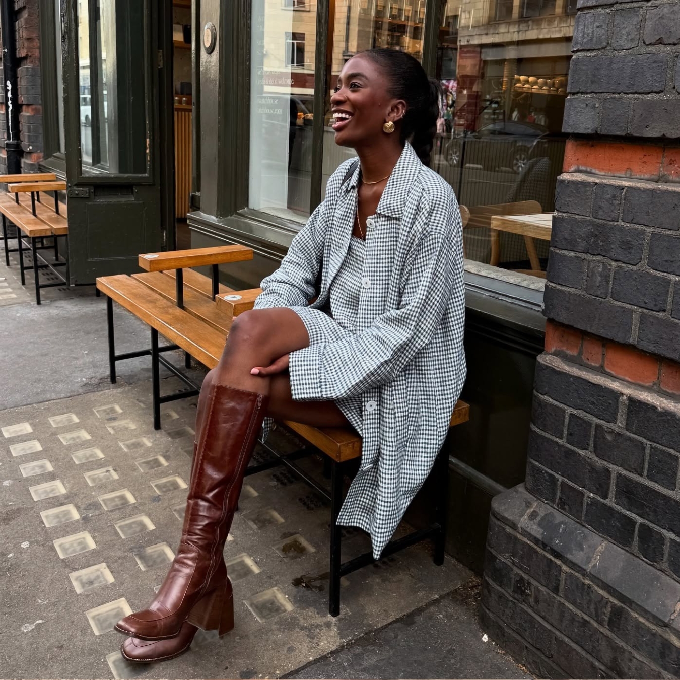 @_livmadeline wearing a gingham dress, jacket and brown leather knee boots.