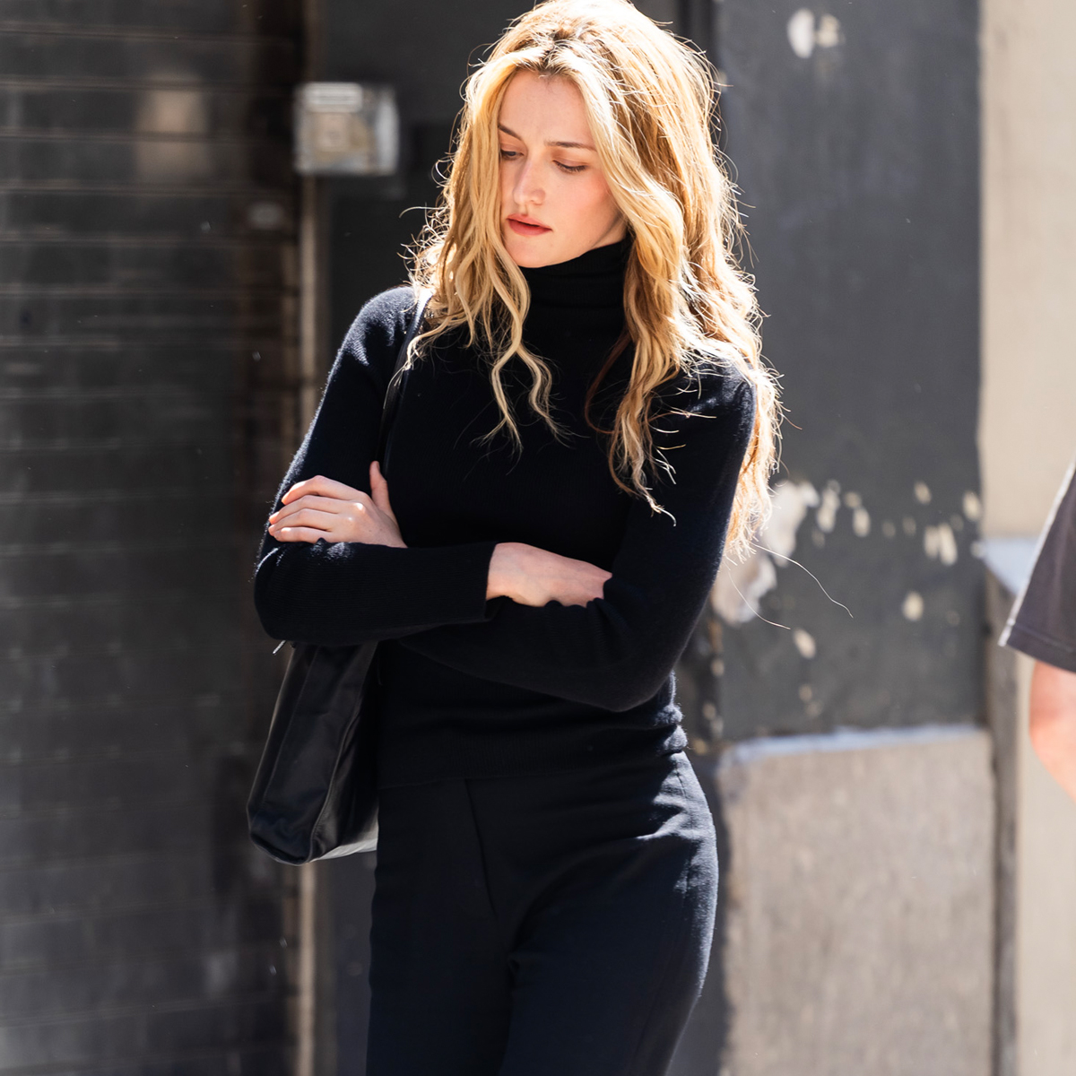 Sarah Pidgeon in character as she portrays Carolyn Bessette-Kennedy in the upcoming series American Love Story, wearing black cropped trousers, black loafers and a black roll neck knit