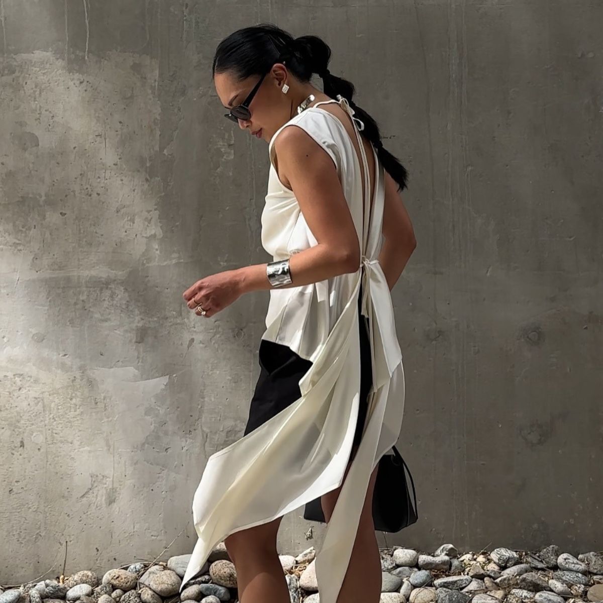 Woman wears cream trousers, a blue shirt and carries a brown The Row Margaux leather tote bag