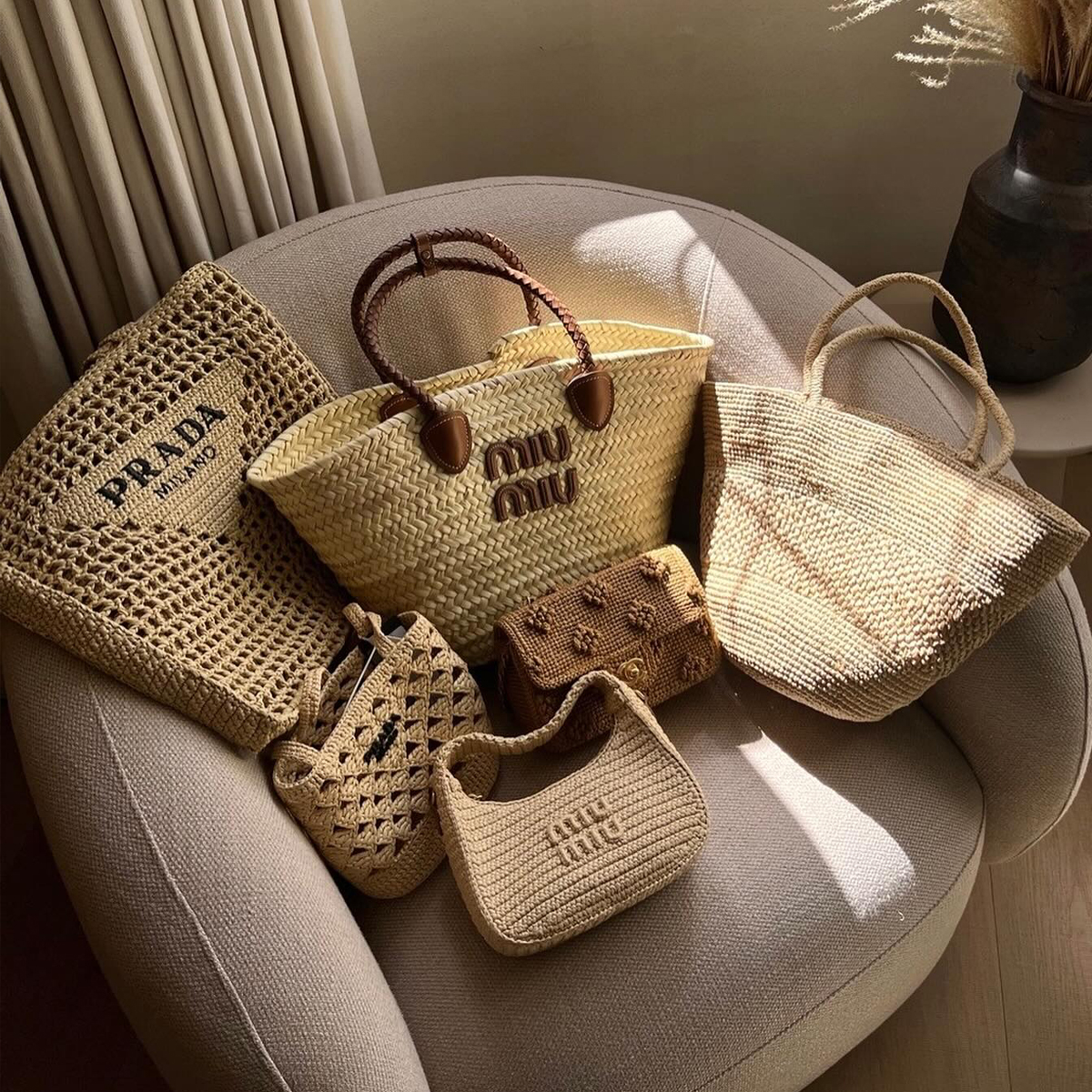 A selection of designer basket bags sit on top of a pink armchair